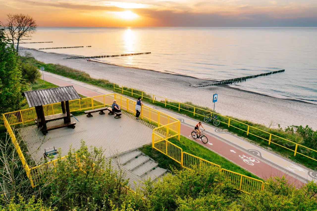 Zachód słońca nad morzem, deptak Grzybowo atrakcje: ścieżka rowerowa, plaża, ławki i wiatka.
