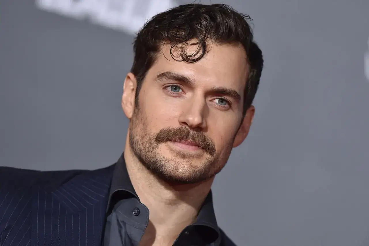 Un homme au regard intense, avec une moustache bien taillée, porte un costume sombre.