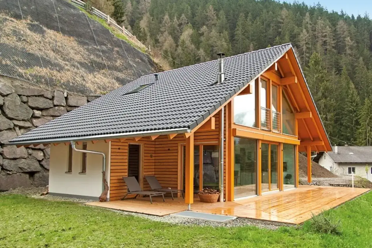 Casa moderna con ampi **tetti in legno** e vetrate, immersa nel verde di un bosco.