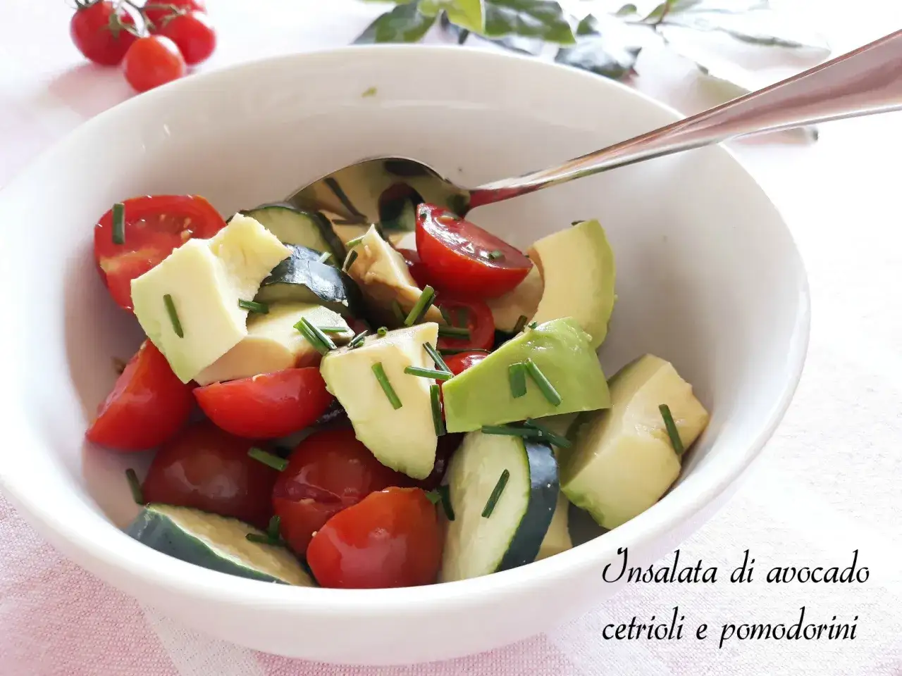 Insalata di avocado, cetrioli e pomodorini freschi, guarnita con erba cipollina, servita in una ciotola bianca.