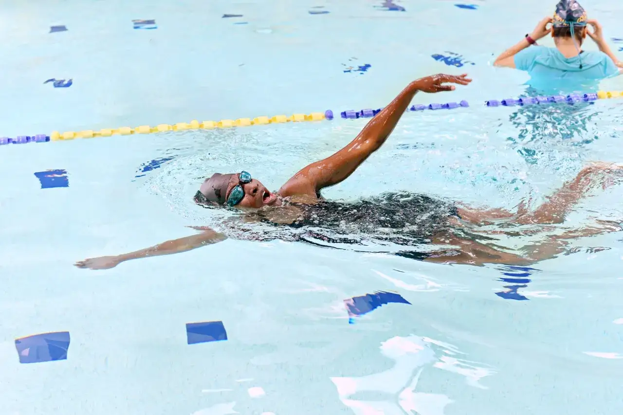 Une nageuse concentrée exécute un mouvement de nage brasse dans une piscine, avec une autre nageuse en arrière-plan.