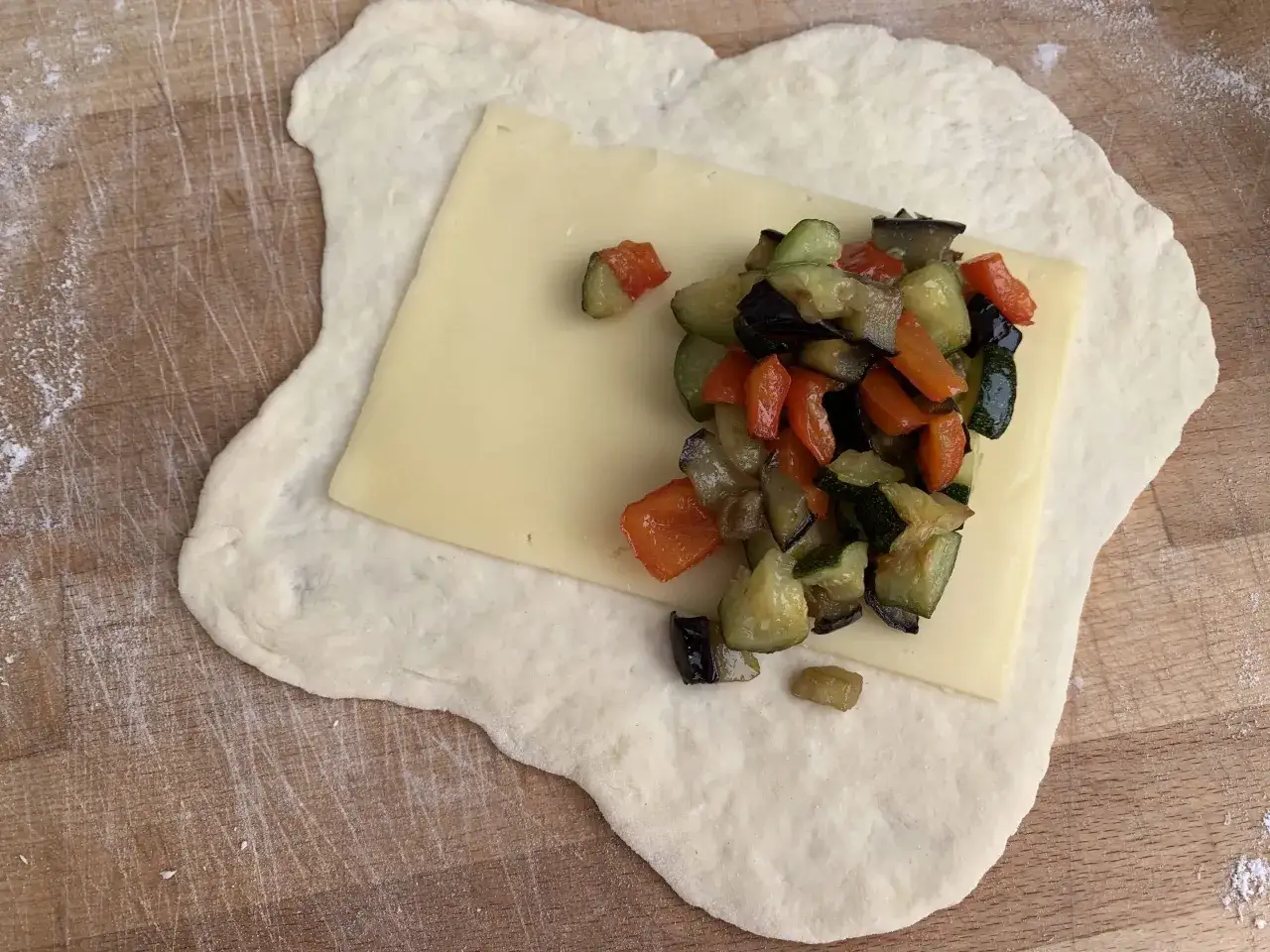 Impasto steso con formaggio e verdure miste, pronto per diventare panzerotti al forno.