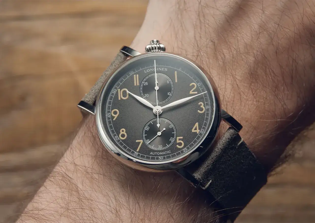 En n&auml;rbild p&aring; ett Longines-ur med gr&aring; urtavla och guldf&auml;rgade siffror, monterat p&aring; en arm. Ett perfekt ur f&ouml;r den som vill ha koll p&aring; tiden.