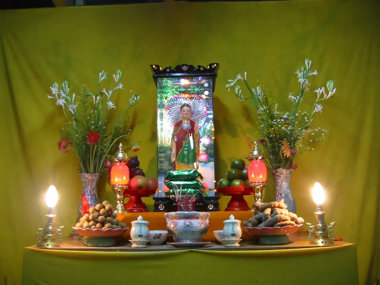 En buddhistisk puja med en Buddha-staty, blommor, frukter och ljus.