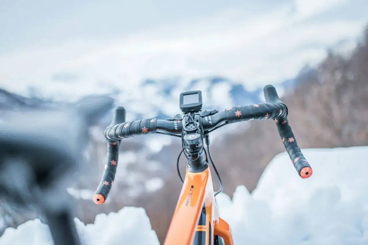 Kierownica roweru z pomarańczowymi akcentami i wzorem płatków śniegu, gotowa na zimowe trasy. Opony zimowe do roweru zapewnią przyczepność na śniegu.