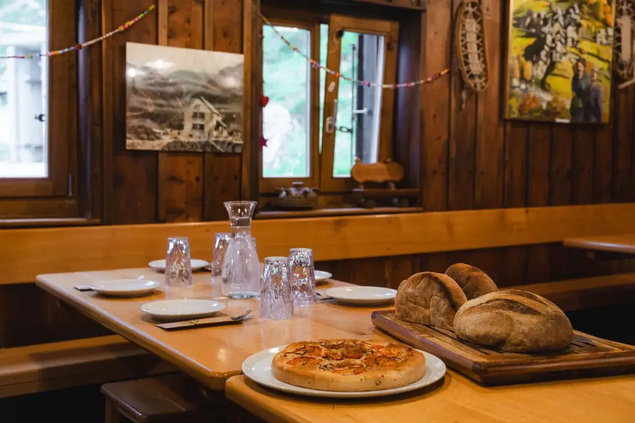 Przytulny nocleg w schronisku. Na drewnianym stole czeka pizza, świeży chleb i nakrycia.