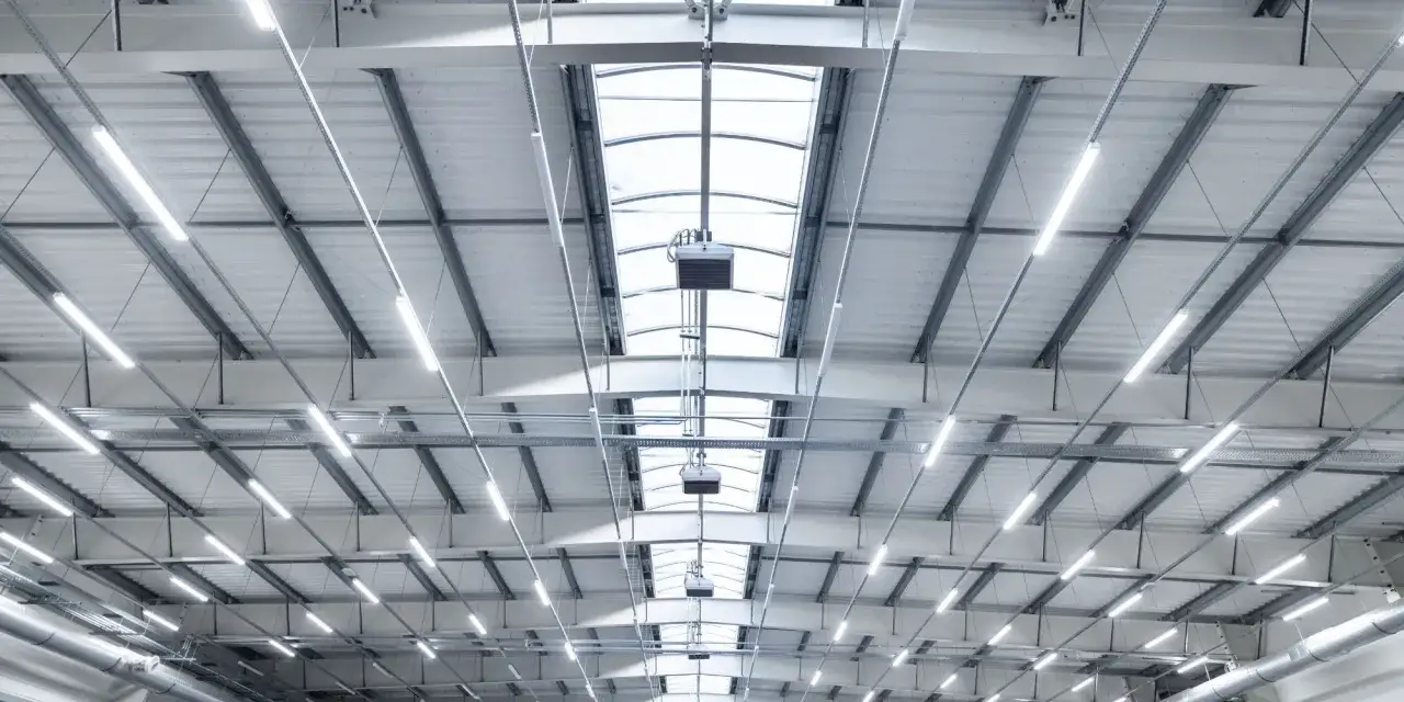 Wielkie hale magazynowe z rzędami nowoczesnych lamp LED i świetlikami dachowymi. Przeprowadzono audyt oświetlenia, by zapewnić optymalne warunki.