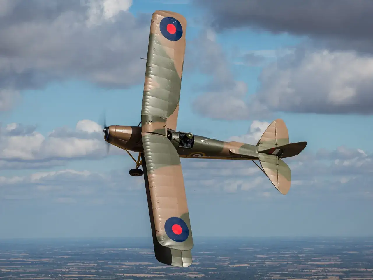 Ein Tiger Moth Flugzeug fliegt im Sonnenschein über eine Landschaft.