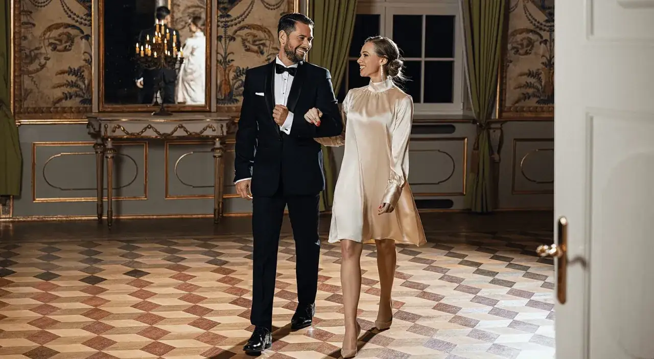 Elegancka para na domówce. On w smokingu, ona w satynowej sukience. Idealne inspiracje, co ubrać na sylwestra na domówkę.