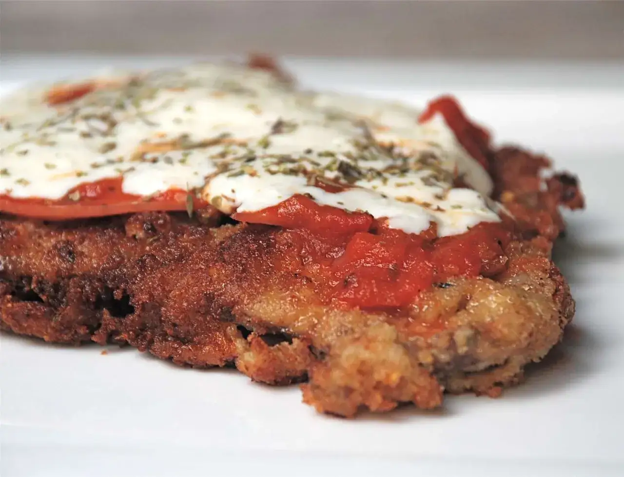 En n&auml;rbild av en saftig milanesa napolitana med sm&auml;lt ost, tomats&aring;s och &ouml;rter.