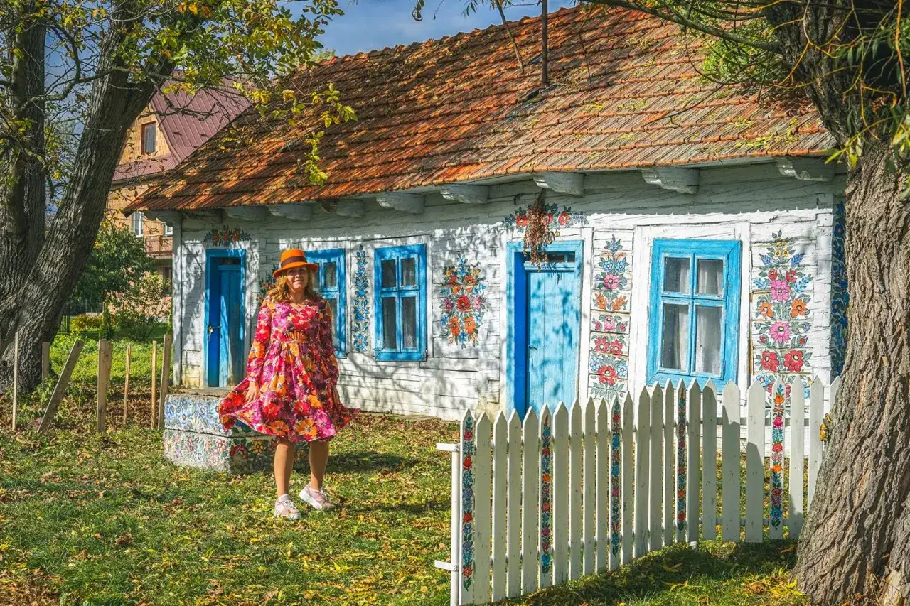 Kobieta w kolorowej sukience pozuje przed malowanymi domami w Zalipiu. Wioska zachwyca ludowymi wzorami.