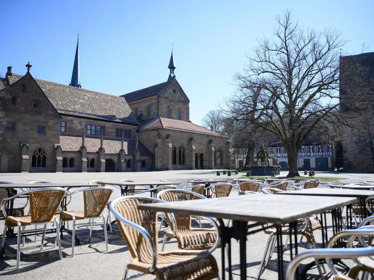 Ein **Kloster** im **mittelalter**lichen Stil mit Kirchturm und einem Innenhof, auf dem leere Tische und St&uuml;hle stehen.