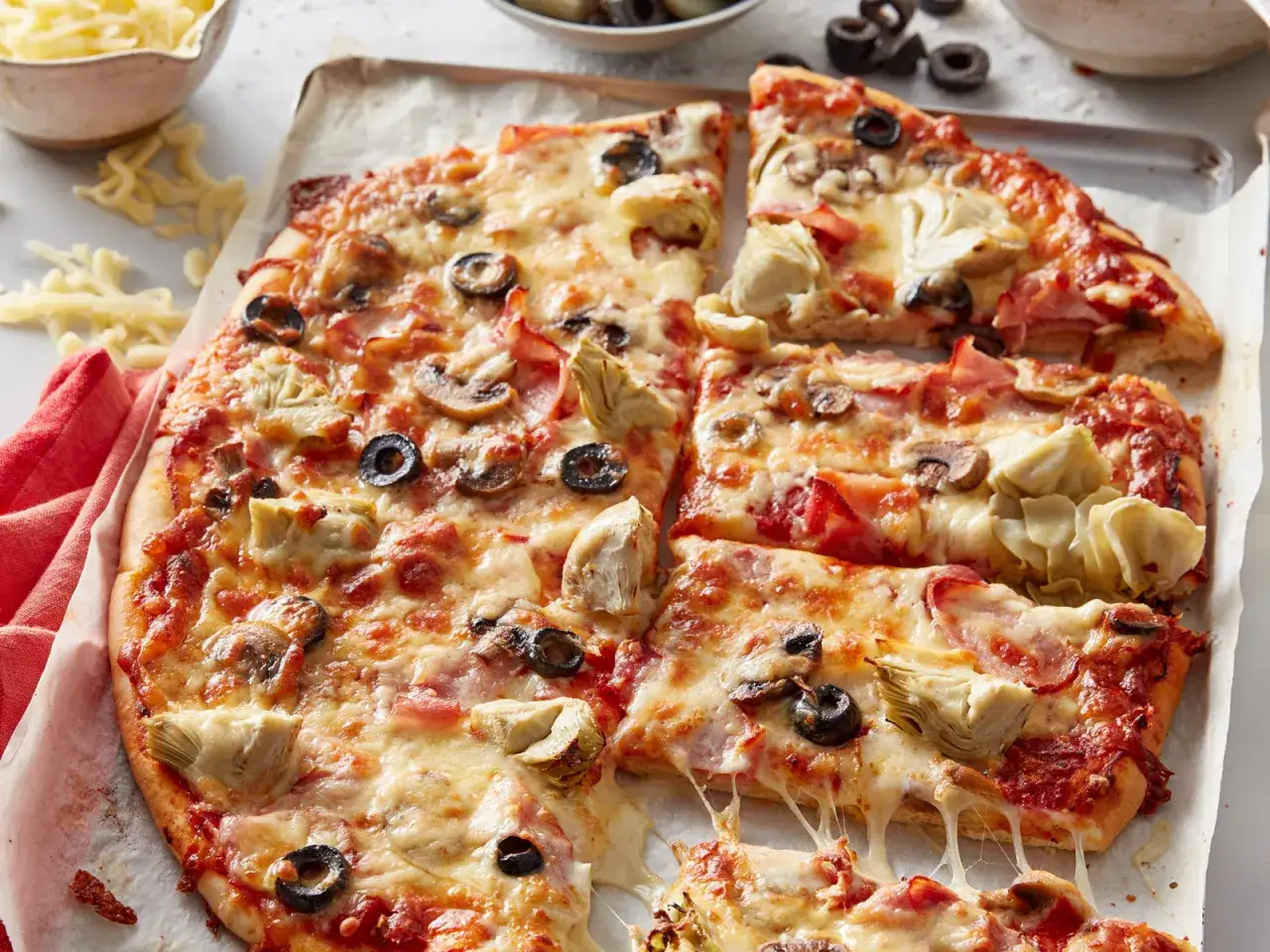 Pyszna pizza capricciosa z roztopionym serem, oliwkami, pieczarkami i karczochami, pokrojona na kawałki.