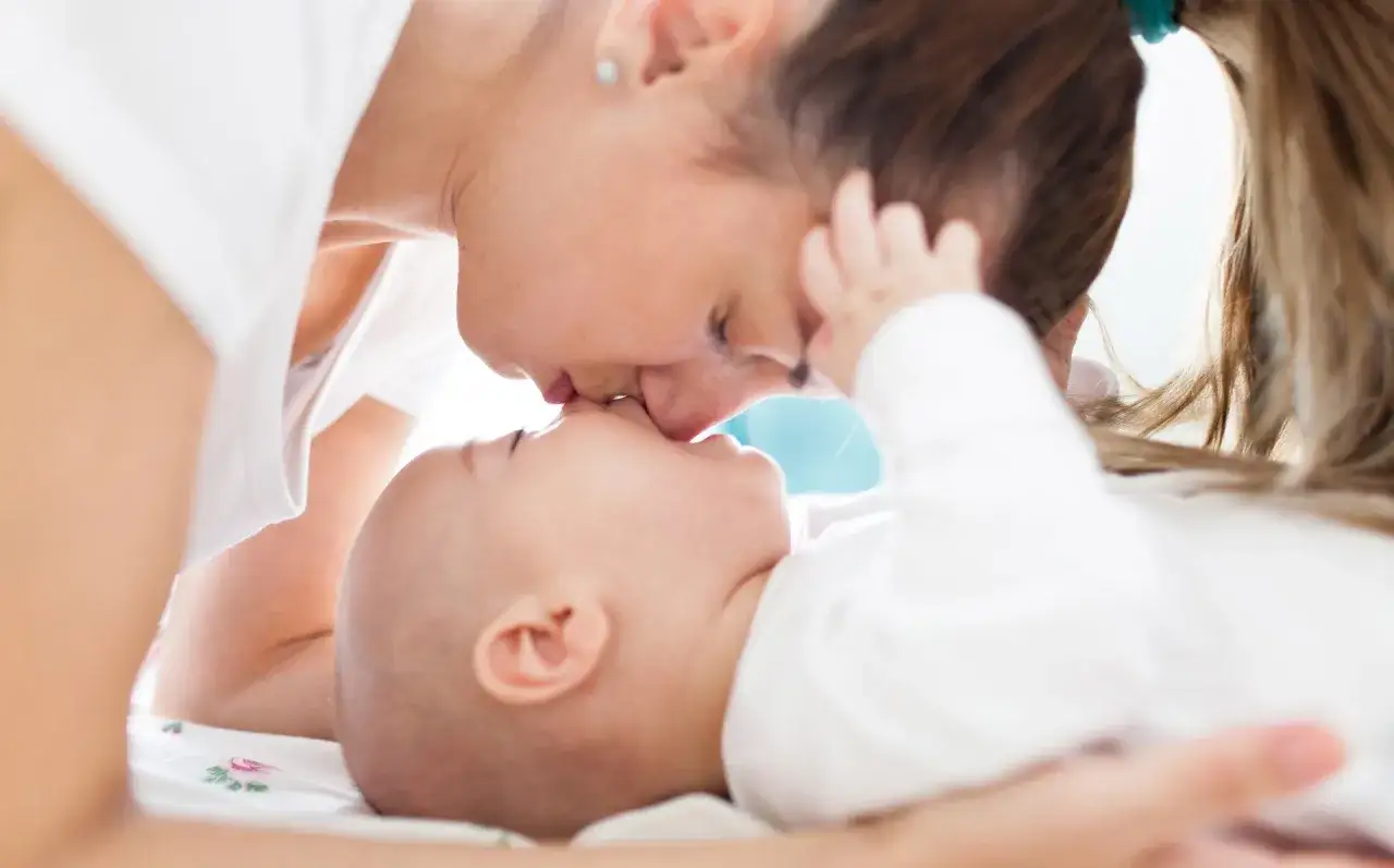 Ciepły uścisk mamy i jej 5 tygodniowe dziecko. Ich twarze są blisko siebie, widać miłość i czułość.