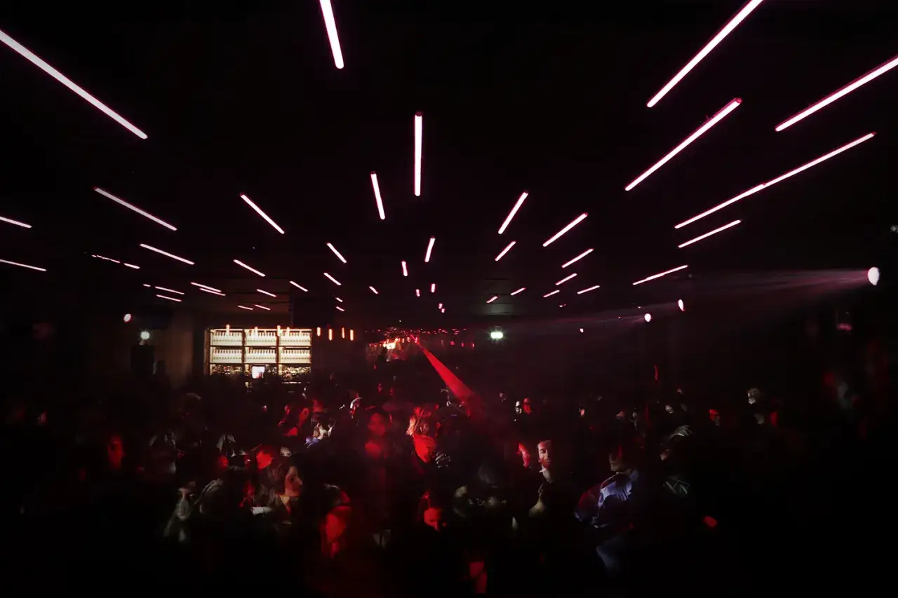 Folla in un locale notturno, luci rosa al neon sul soffitto e fumo. Un'atmosfera vibrante per gli eventi di musica elettronica a Milano.