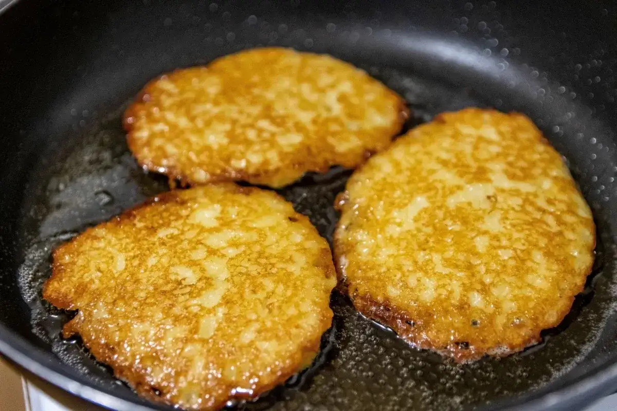 Złociste placki bez jajek smażą się na patelni, tworząc apetyczny obraz domowego obiadu.