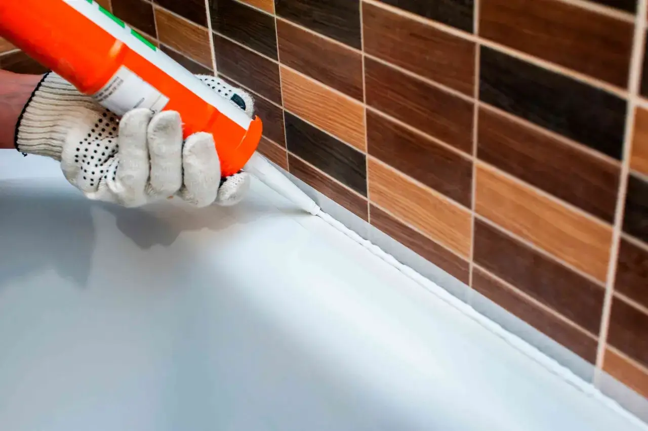 Aplicando sellador para evitar humedad en pared contigua a la ducha.