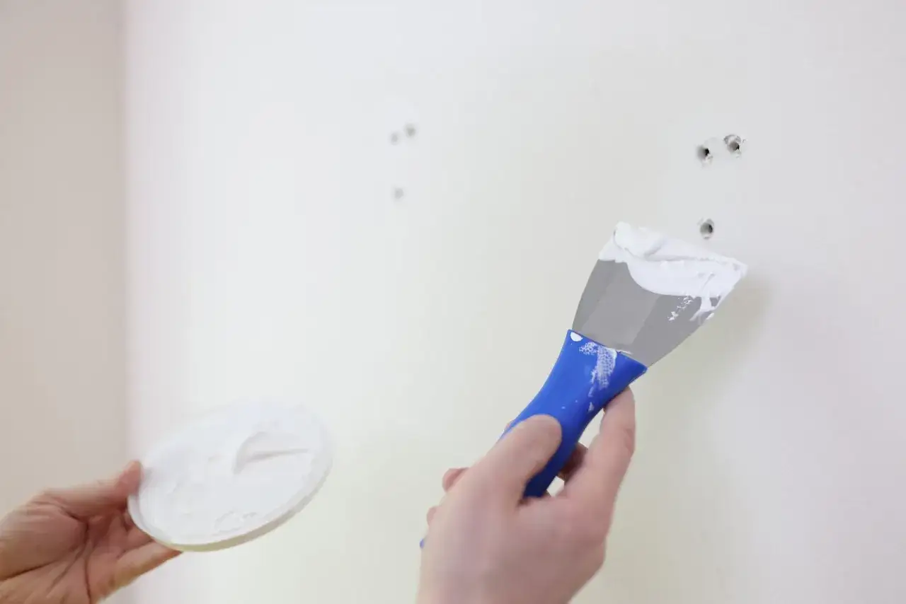 Mano aplicando masilla con esp&aacute;tula para alisar paredes y reparar agujeros.