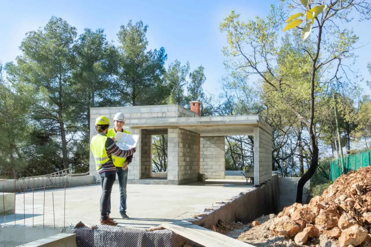 Deux hommes discutent des plans sur un chantier. Le contrat général évalue l'avantage inconvénient de chaque étape.