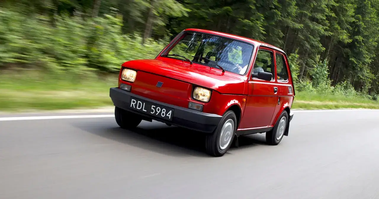 Czerwony Fiat 126p, mimo swojego wieku, prezentuje się elegancko, pędząc leśną drogą.