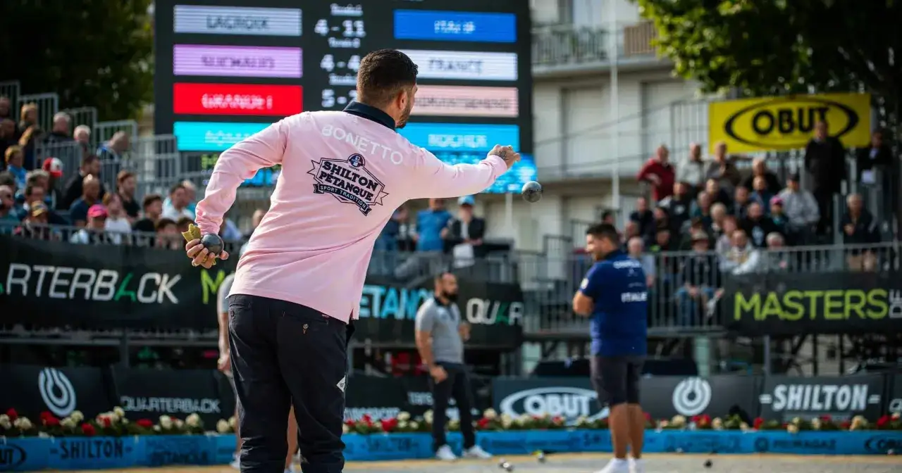Un joueur lance une boule lors d'une comp&eacute;tition de p&eacute;tanque. Le public est derri&egrave;re les barri&egrave;res.