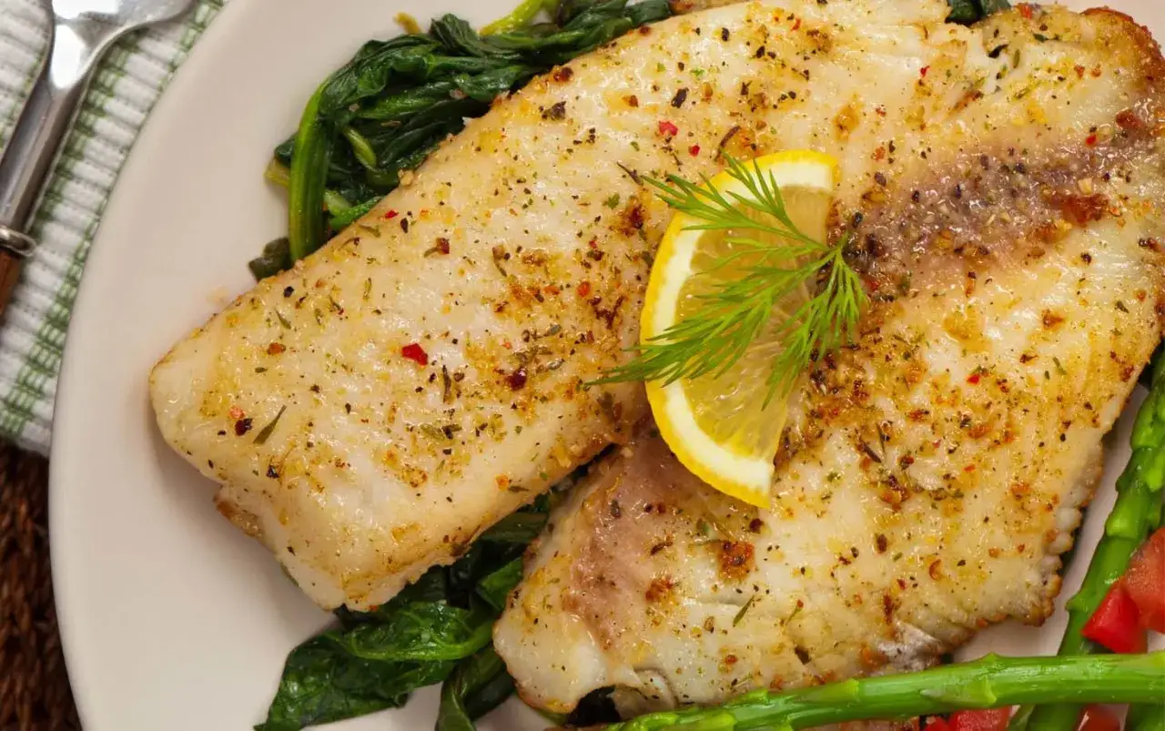Dos filetes de tilapia sazonados, servidos sobre espinacas y esp&aacute;rragos, con una rodaja de lim&oacute;n y eneldo.