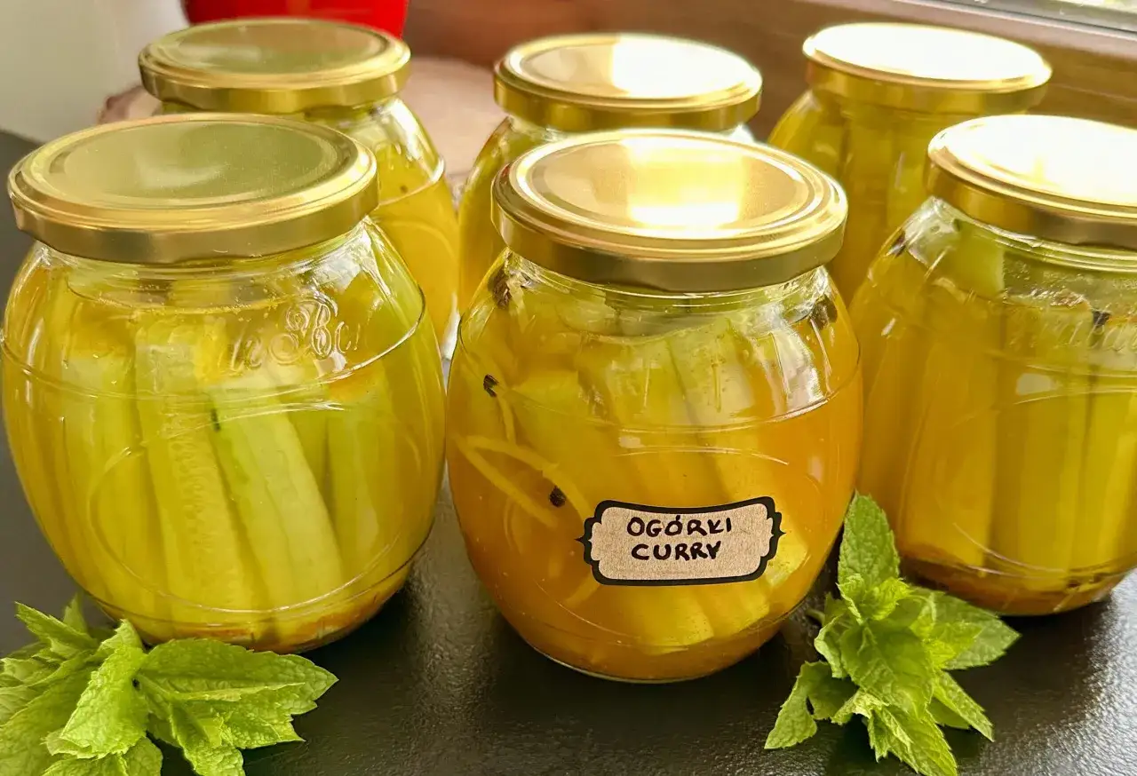 Słoiki z ogórkami w zalewie curry, ozdobione świeżą miętą. Idealne na przetwory.