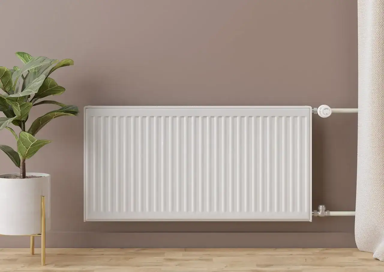 Instalaci&oacute;n de radiadores: un radiador blanco moderno junto a una planta en maceta y una cortina, listo para calentar el hogar.