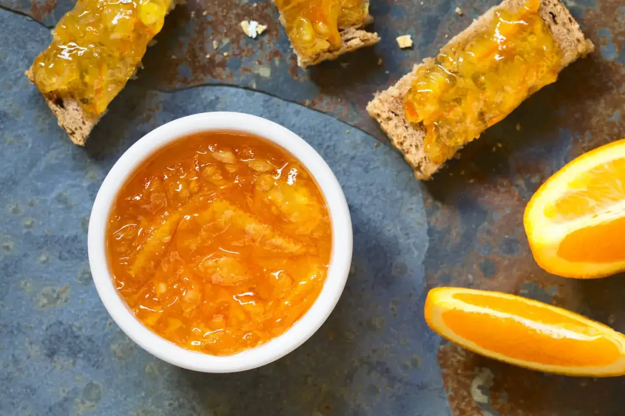 Confiture d'&eacute;corce d'orange brillante dans un bol blanc, servie sur des toasts avec des quartiers d'orange frais.