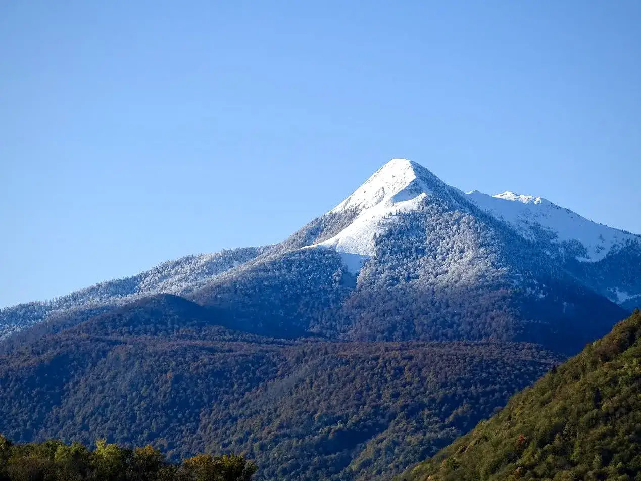 Le pic de Cagire, majestueux et enneigé, domine un paysage de montagnes forestières sous un ciel bleu clair.