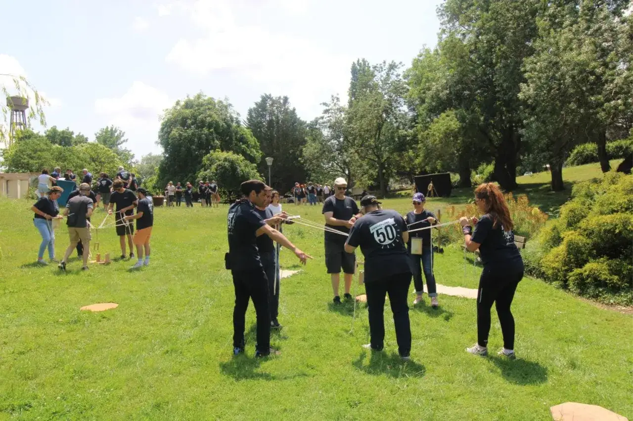 Des participants s'amusent lors d'une activité team building plein air, manipulant des cordes et des blocs de bois dans un parc verdoyant.