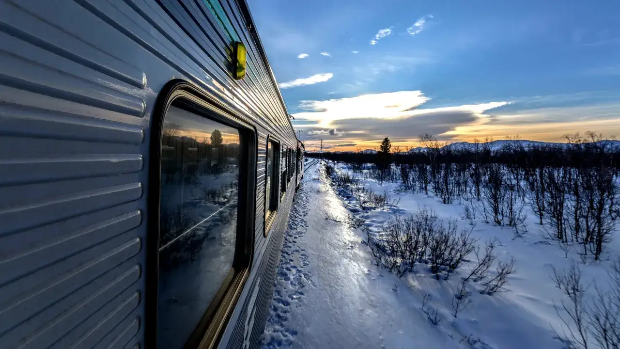 T&aring;get rullar genom ett sn&ouml;igt landskap mot Boden, med en vacker solnedg&aring;ng i horisonten. En resa fr&aring;n Stockholm.