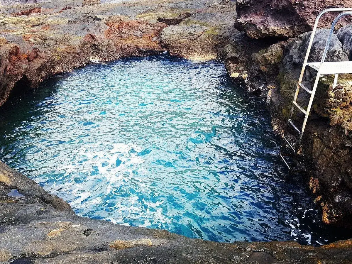 Un charco de los abrigos natural, con aguas cristalinas y una escalera metálica para acceder.
