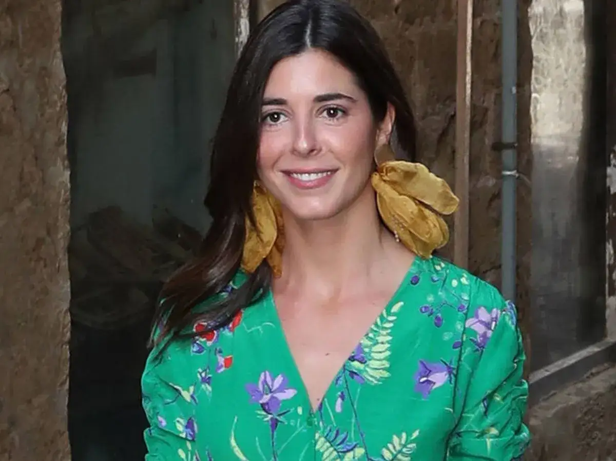 Belen Corsini sonr&iacute;e con pendientes dorados y un vestido verde estampado.