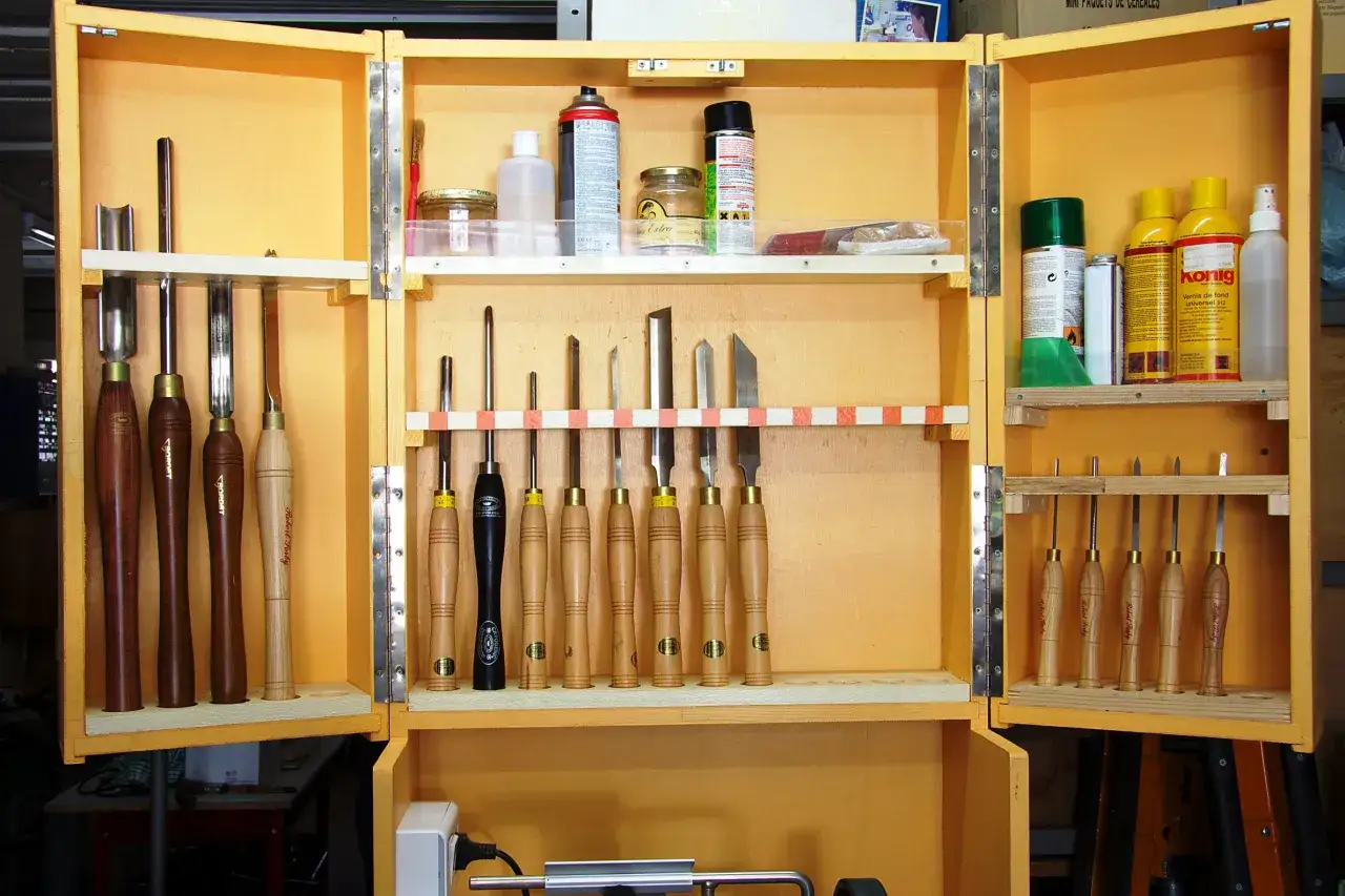 Boîte de rangement jaune ouverte, remplie d'outils pour la sculpture bois, dont des gouges et des ciseaux, ainsi que des produits de finition.