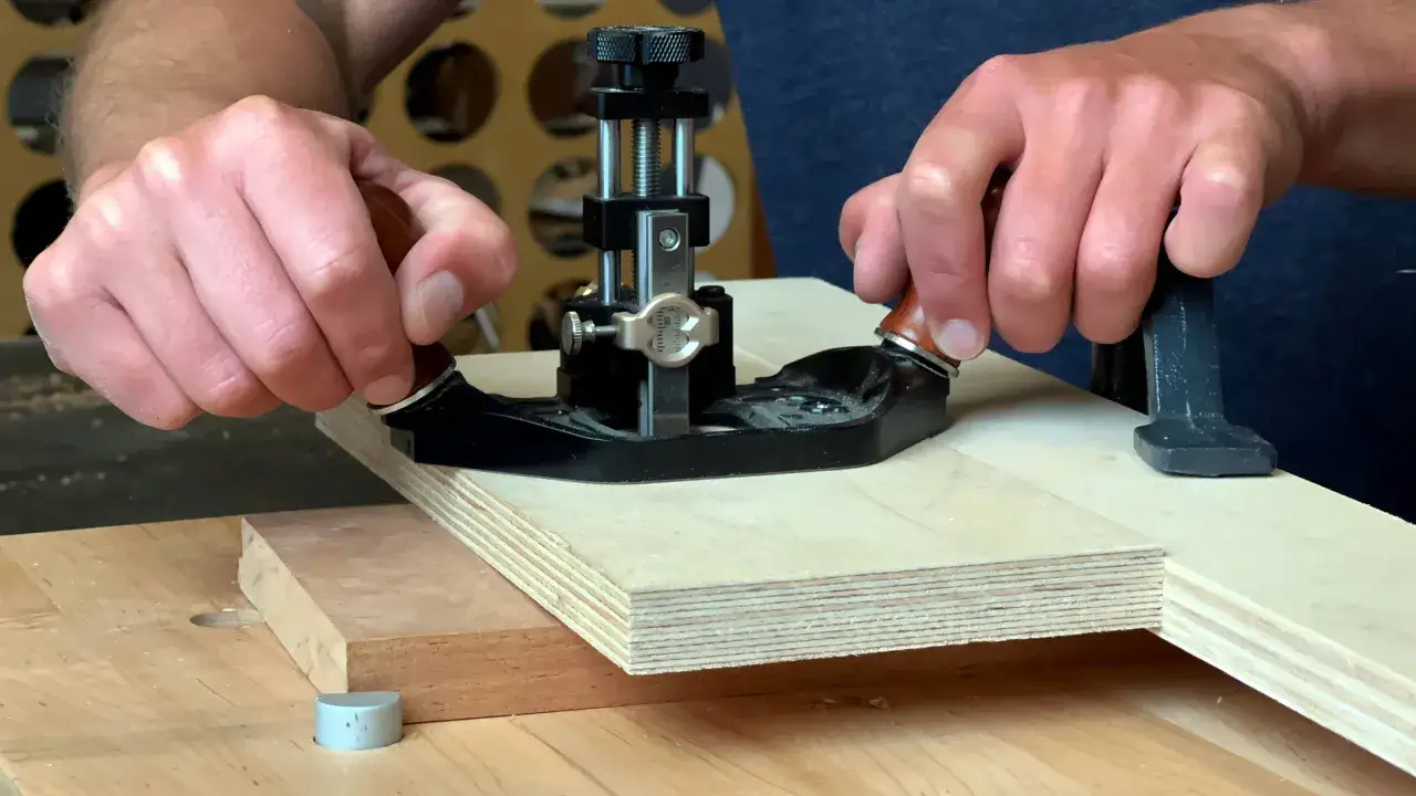 Main d'artisan guidant une défonceuse pour créer une rainure précise sur une planche de contreplaqué.