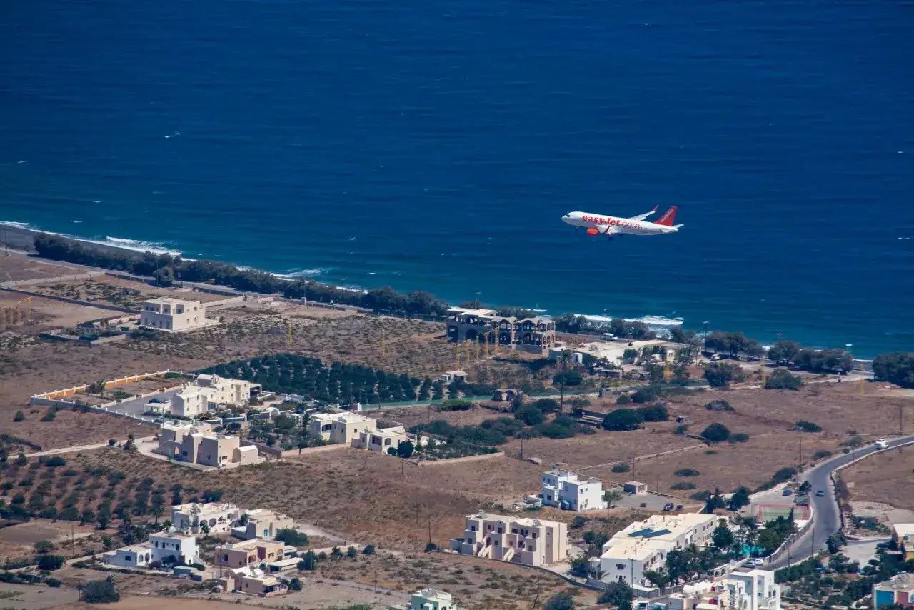 Samolot EasyJet zbliża się do lądowania nad Santorini. Widok z lotu ptaka na białe domy i turkusowe morze.
