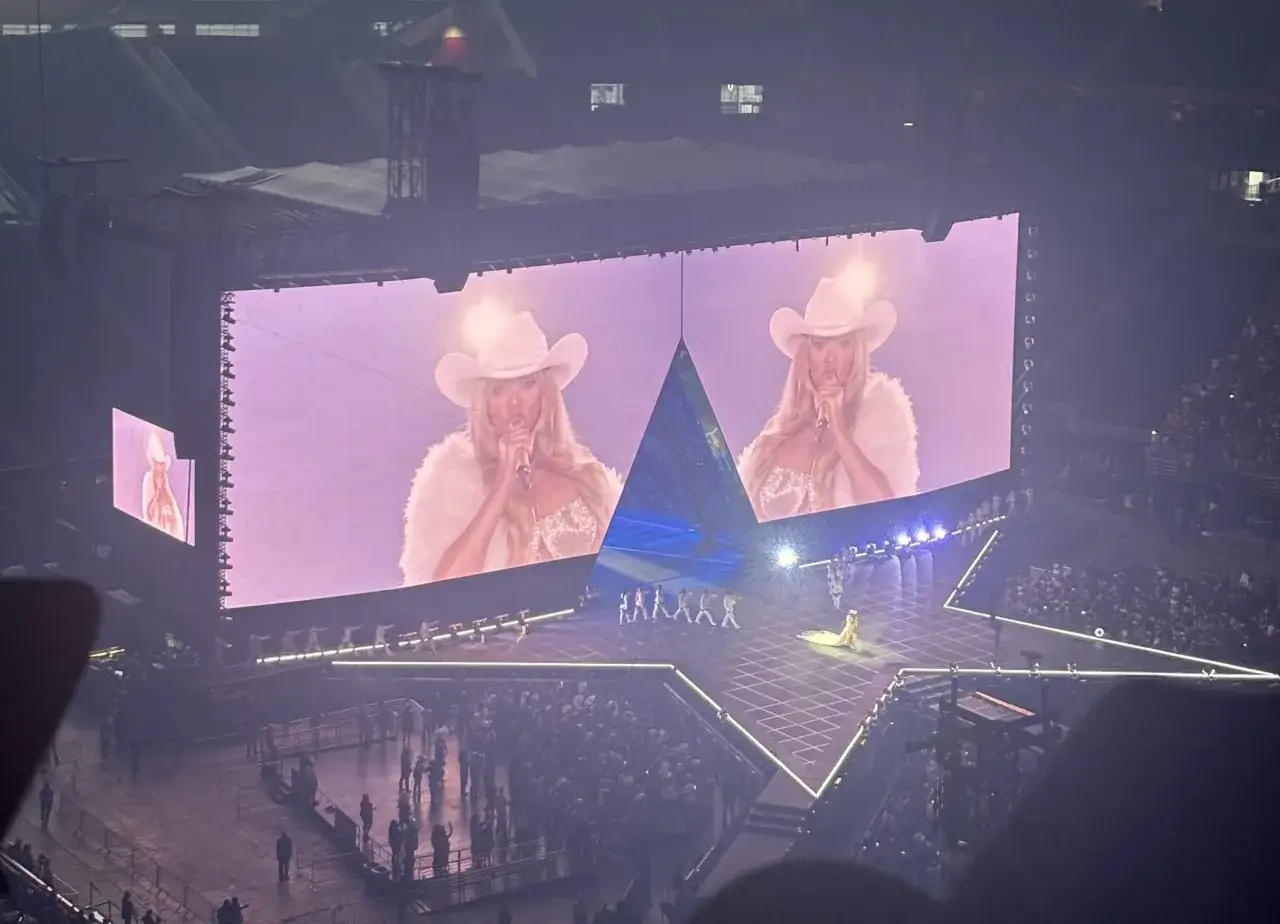Beyonce koncert w kowbojskim kapeluszu na ekranie, z tancerzami na scenie w kształcie gwiazdy.
