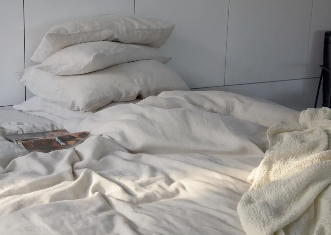 Ein Bett mit Leinenwäsche, frisch gewaschen mit Essig. Kissen stapeln sich, ein Magazin liegt auf der Decke.