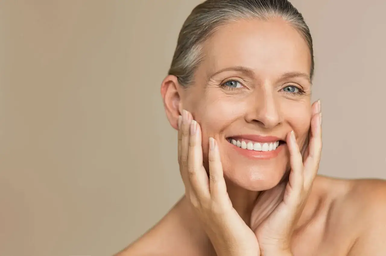 Donna sorridente con pelle matura, accarezza il viso con le mani. La sua pelle matura da che et&agrave; mostra saggezza e bellezza.