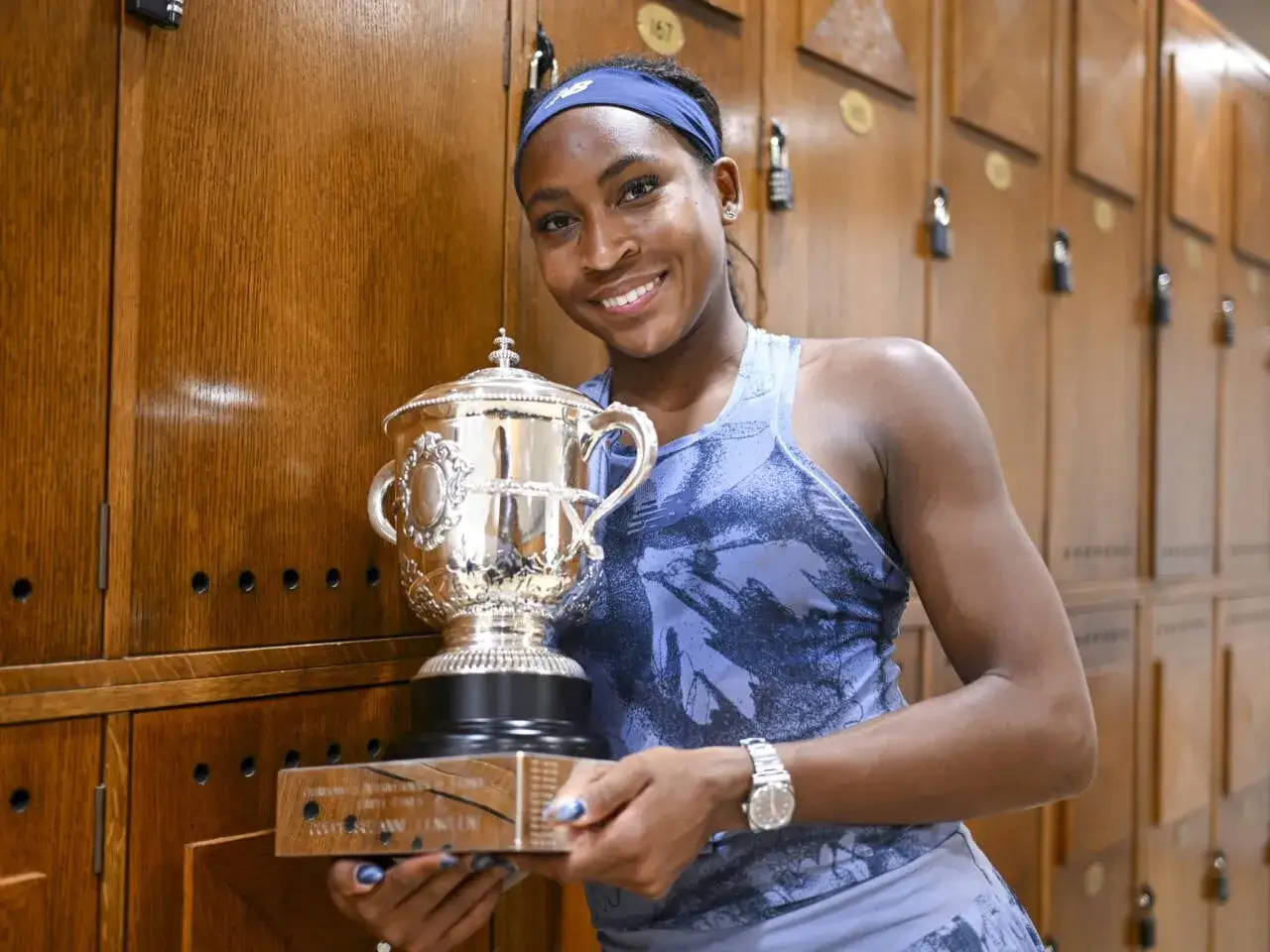 Joven tenista sonr&iacute;e con un trofeo de plata, un s&iacute;mbolo de sus premios Grand Slam, en un vestuario de madera.
