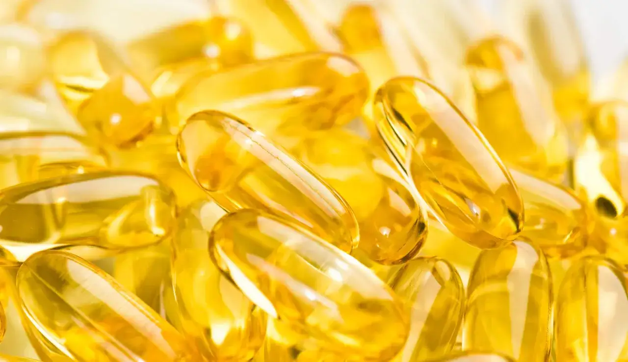 Złote kapsułki z tocopheryl acetate, błyszczące i półprzezroczyste, tworzą gęsty stos.