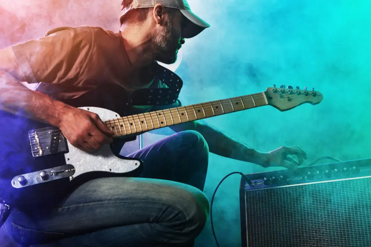 Mann mit Gitarre und Verstärker, der den perfekten gitarren sound sucht. Nebel und bunte Lichter schaffen eine rockige Atmosphäre.