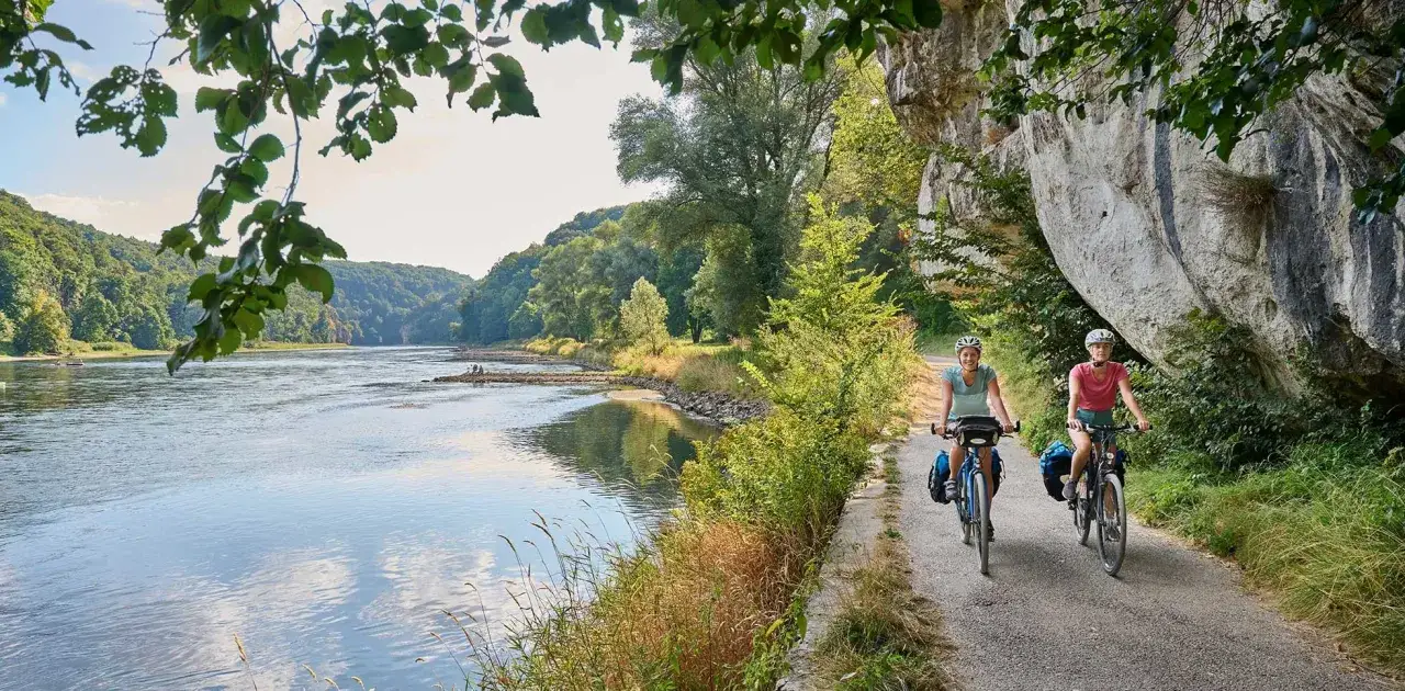 Zwei Radfahrerinnen genie&szlig;en die idyllische Landschaft auf einem der vielen Radwege Bayerns entlang eines Flusses.