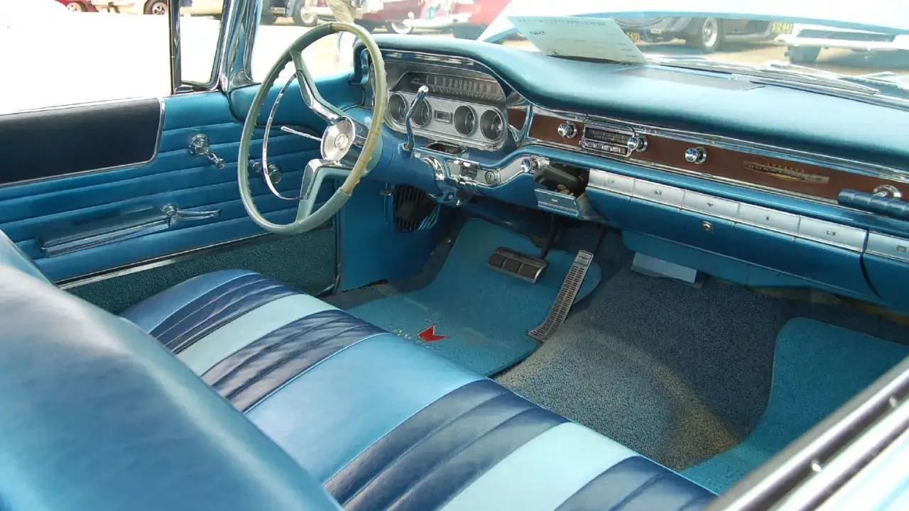Interi&ouml;r i en bl&aring; klassisk bil, kanske en Rover P5, med randiga s&auml;ten och kromdetaljer.