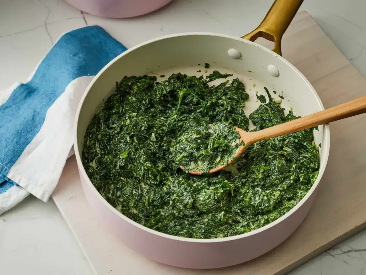 Krämig spenat i en panna, perfekt för ett snabbt spenat recept. En träsked rör om i den gröna delikatessen.