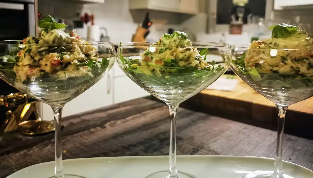 Drei Gläser mit einem leckeren Krabbencocktail mit Avocado und frischen Kräutern, serviert auf einem Bett aus Rucola.