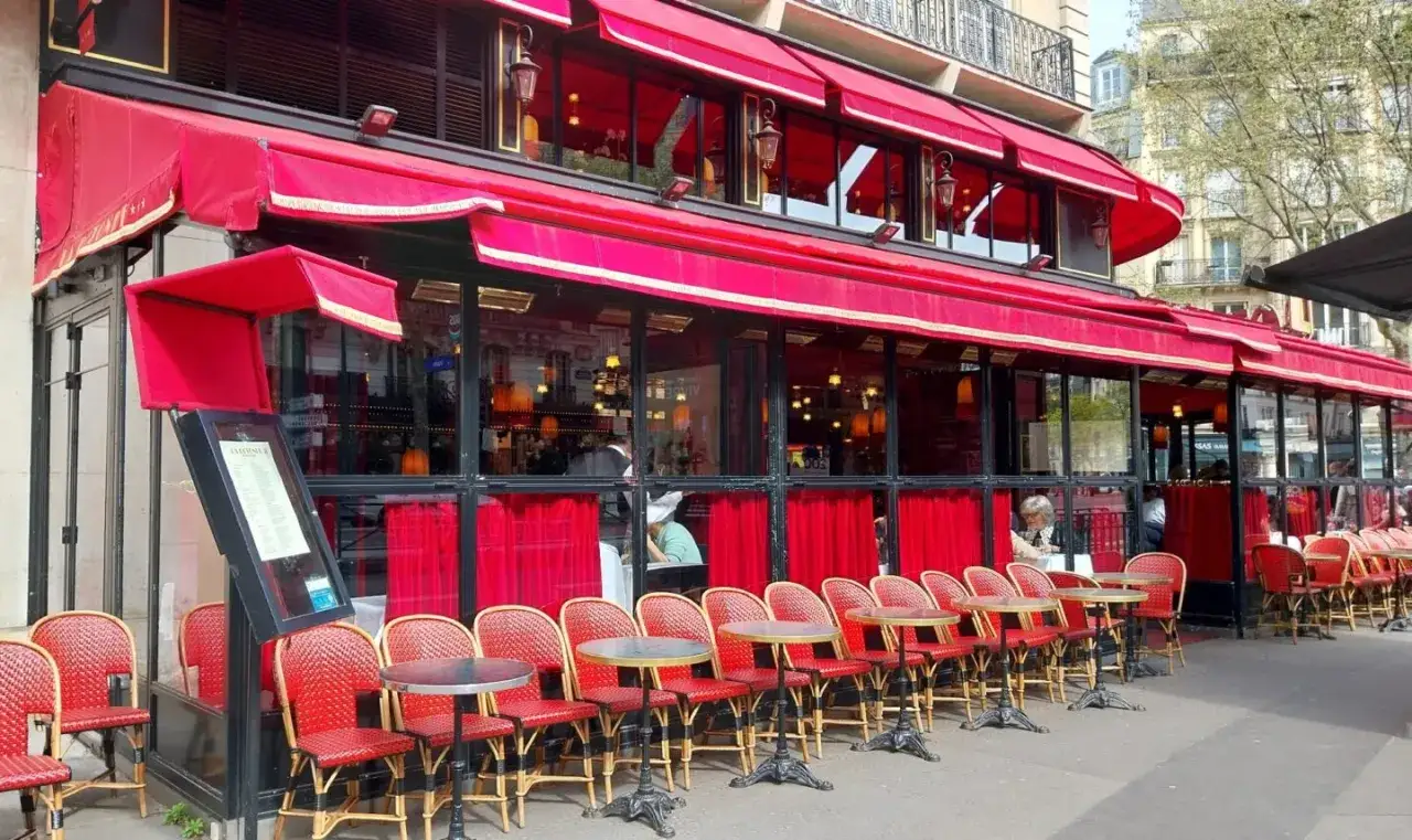 Terrasse d'un restaurant parisien, avec ses chaises rouges et ses tables, sous les auvents rouges. Un menu est visible &agrave; l'entr&eacute;e.