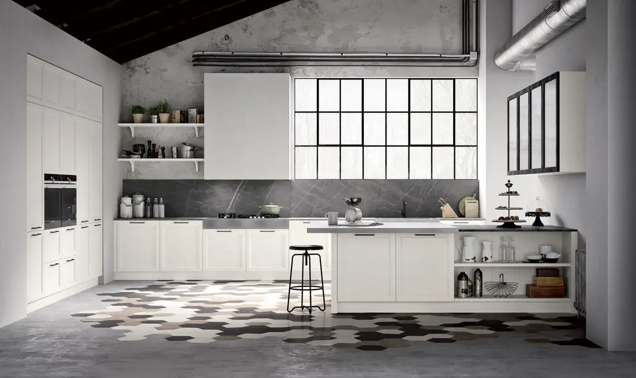 Cucina senza cappa con isola centrale, mobili bianchi, piano in marmo e un grande finestra industriale. Pavimento esagonale colorato.