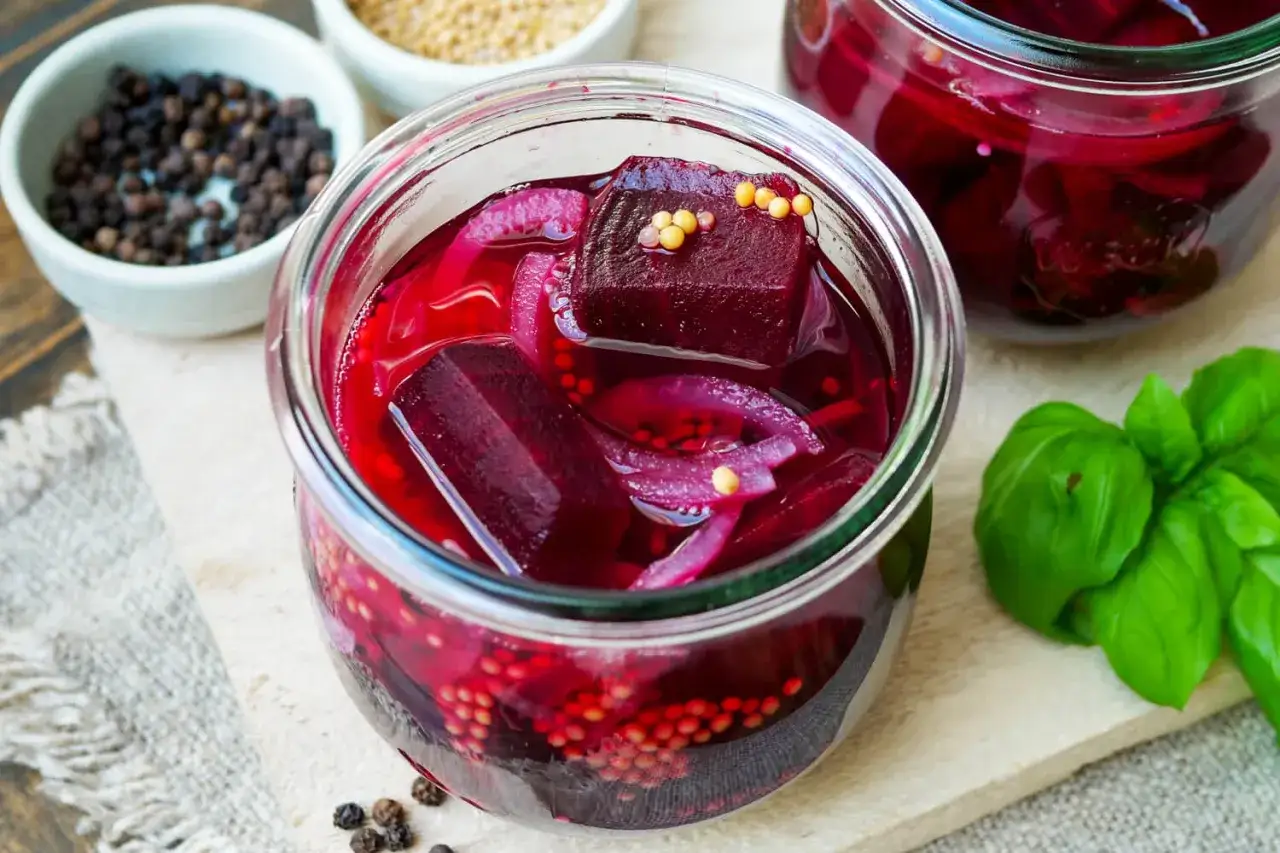Rote Bete haltbar machen: Ein Glas mit eingelegter Rote Bete, Zwiebeln und Senfk&ouml;rnern. Daneben Sch&uuml;sseln mit Pfeffer und Senfk&ouml;rnern.